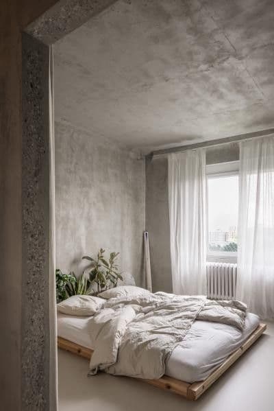 Minimalist bedroom with concrete-textured microcement walls and bright natural lighting