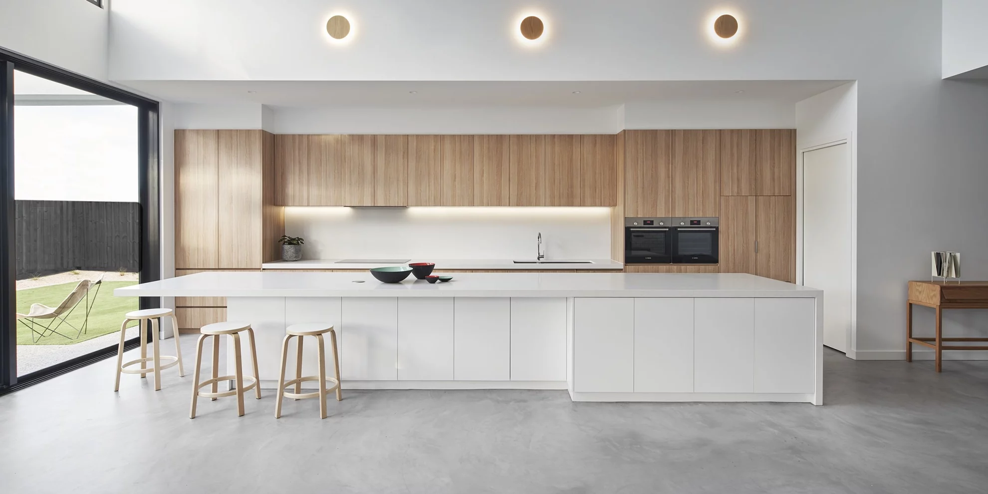 Monolithic light grey microcement floor and white minimalist island in a luxury modern kitchen, highlighting the seamless grout-free finish and industrial durability.