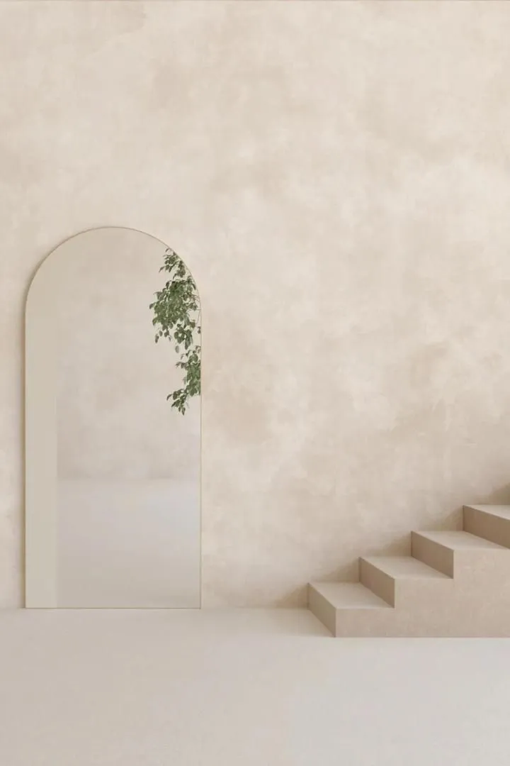Seamless microcement wall finish along a minimalist staircase with an arched mirror.