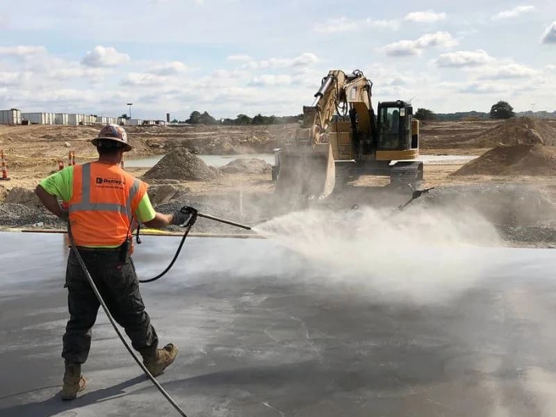 Worker spraying water for concrete curing process in Saudi Arabia construction site
