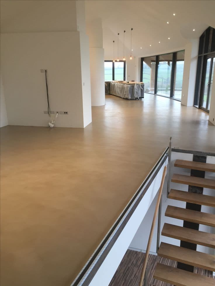 Large scale open-plan living area featuring a seamless beige microcement floor system with integrated staircase transitions.