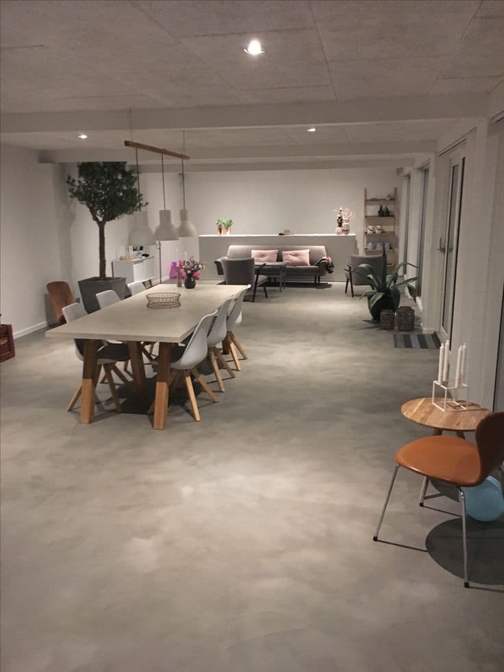 Textured mineral microcement flooring in a modern dining space, showing superior light reflection and grout-free continuity.