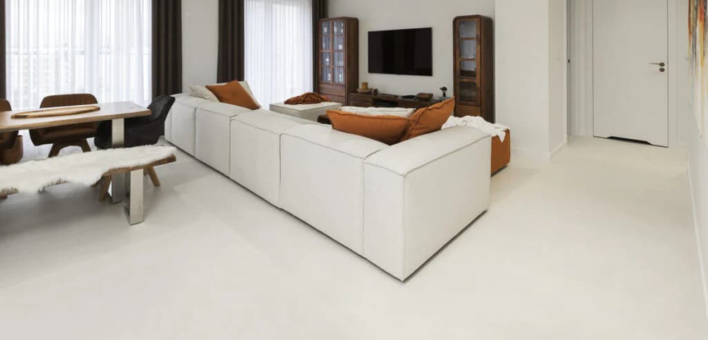 Monolithic white microcement flooring in a minimalist open-plan living and dining area, highlighting the seamless continuity and superior light-reflectance of the architectural mineral finish.