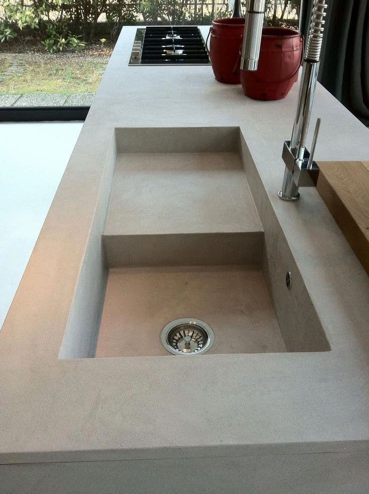 Close-up of an integrated microcement kitchen sink molded seamlessly into the countertop to eliminate dirt-trapping edges.