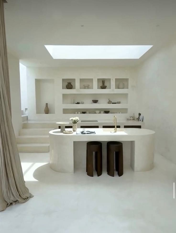 Monolithic white microcement kitchen island with an oval design, showcasing a seamless and architectural mineral skin.
