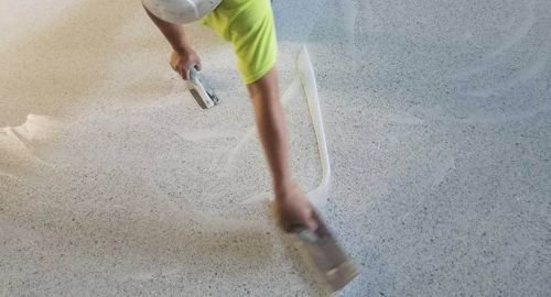 Worker in orange jacket troweling freshly poured terrazzo flooring in a Jeddah construction site, ensuring even curing for Saudi Arabia’s extreme heat.